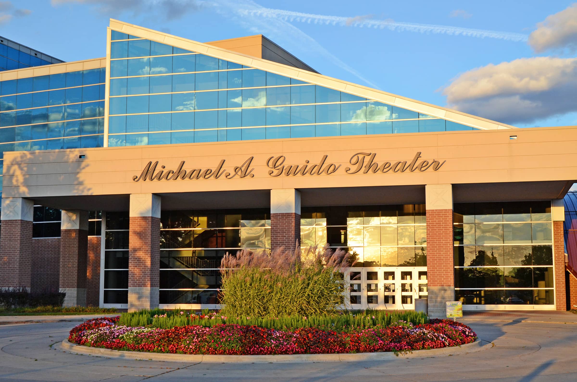 Entrance of Michael A. Guido Theater featuring large glass windows and a flower bed in front.